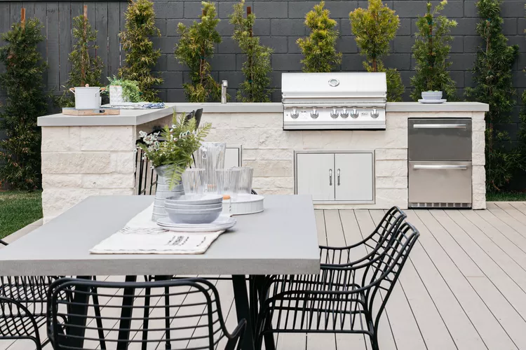 Outdoor Kitchen With Grill, Countertops, And Seating Area In A Beautiful Backyard Setting.